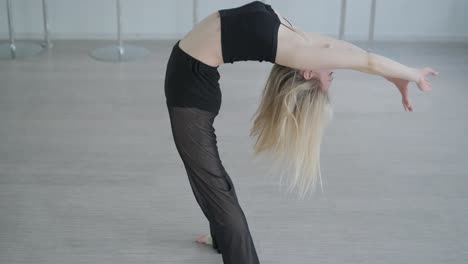 fit girl in black clothes performing contemporary. female dancer shows flowing motions, body and hands waves at white room. modern ballet dance choreography. young woman is moving smoothly