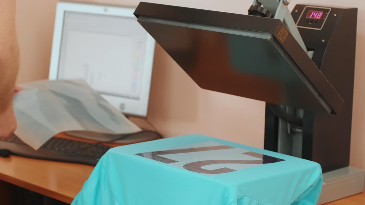 나무 테이블에 티셔츠와 함께 열 프레스 기계. 노동자는 높은 온도 티셔츠에 숫자를 적용하기 위해 손 프레스를 누릅니다.