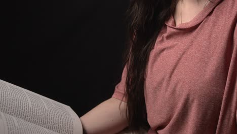 a woman sits peacefully, reading a book against a dark background. the soft lighting creates a dramatic, intimate atmosphere, highlighting her focus and calm demeanor