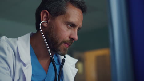 Bearded-therapist-listening-heartbeat-of-unknown-patient-in-clinic-ward-portrait