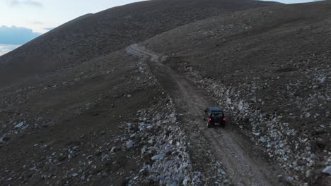 Video-De-Drones-Siguiendo-El-Seguimiento-De-La-Conducción-De-Automóviles-Fuera-De-La-Carretera-En-Un-Camino-De-Tierra-De-Montaña-Rocosa-En-El-Monte-Olimpo-Grecia-Al-Atardecer