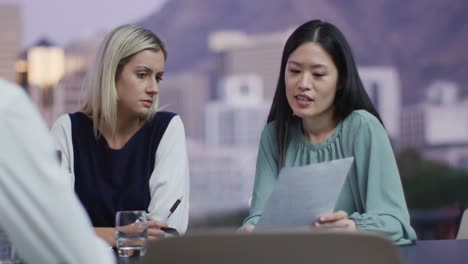 Video-of-two-diverse-female-colleagues-discussing-document-at-evening-office-meeting