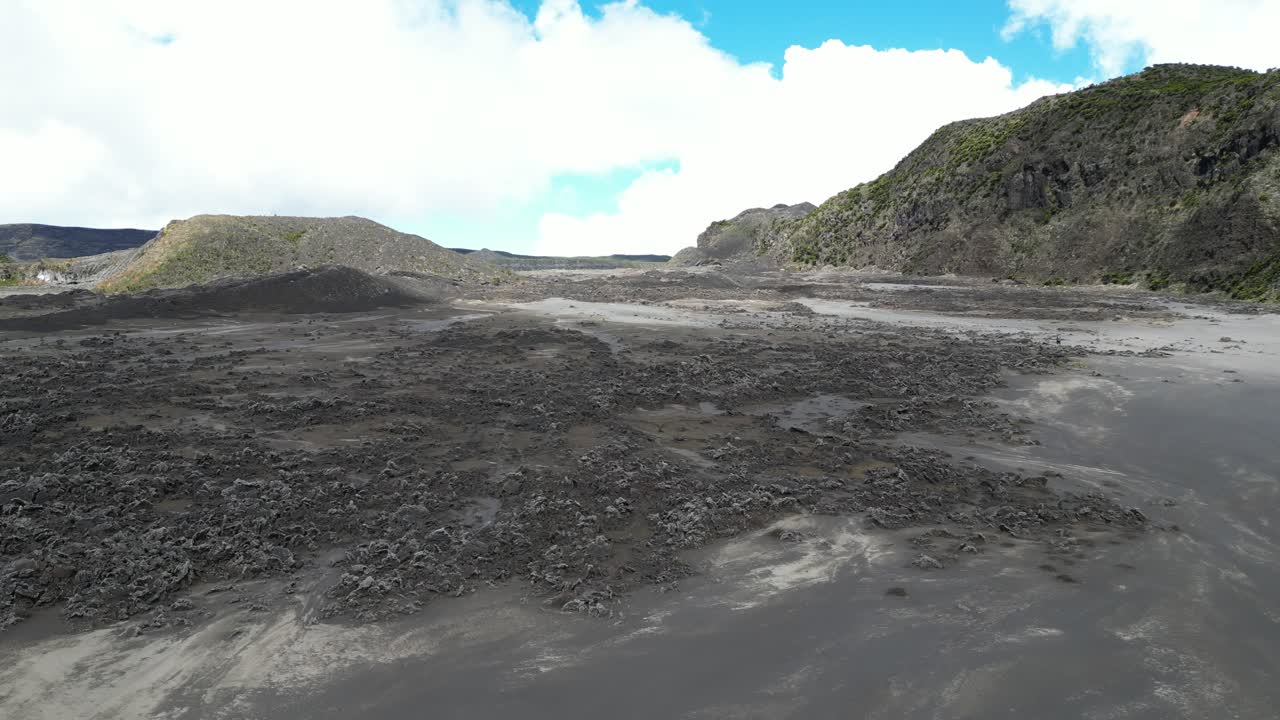 volando sobre terreno cubierto de ceniza volcánica negra, cráter volcánico con colina en el horizonte, islas comoras