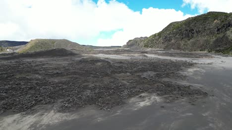 flying over terrain covered with black volcanic ash, volcanic crater with hill in horizon, comoros islands