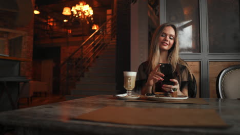 Hermosa-Y-Emocional-Chica-Feliz-Está-Haciendo-Fotos-De-Comida-En-La-Cafetería,-Café-Con-Leche-En-La-Mesa,-Postre-Helado-Pastel-De-Chocolate-Cereza-Menta,-Comunicación-En-Redes-Sociales