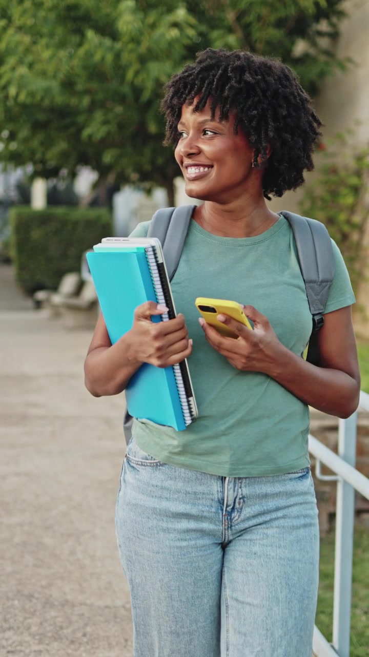 Smiling African American Student Walks on Campus Using Smartphone