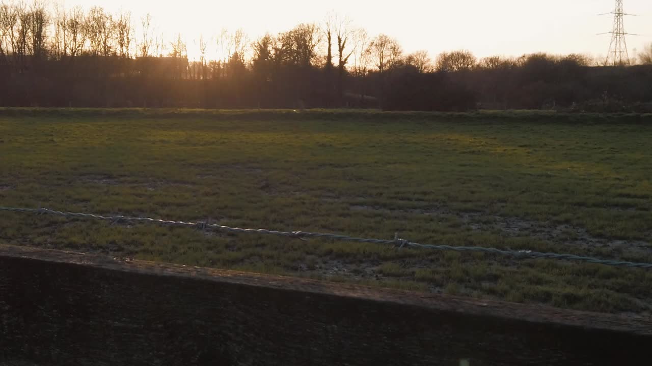 Slow motion Tracking dolly shot of sunset sunnrise across a grass field with silhouette of trees and fence