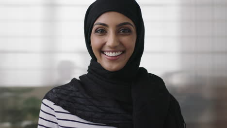 portrait of professional young muslim business woman looking at camera laughing cheerful wearing traditional headscarf in office background