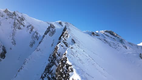 the-camera-flies-along-a-crest-with-snow-covered-white-mountains