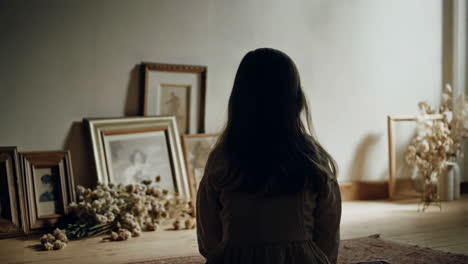 child sitting on floor amidst framed pictures and dried plants
