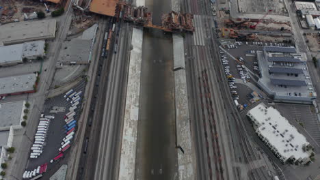 AERIAL:-Overhead-,-Birds-Eye-View-on-Los-Angeles-River-with-Water-on-Cloudy-Overcast-Sky-next-to-Train-Tracks