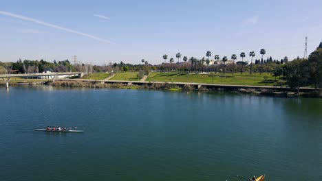 Drone-flight-crossing-the-Guadalquivir-river-and-where-two-canoes-are-training,-crossing-each-other-in-the-video-shot