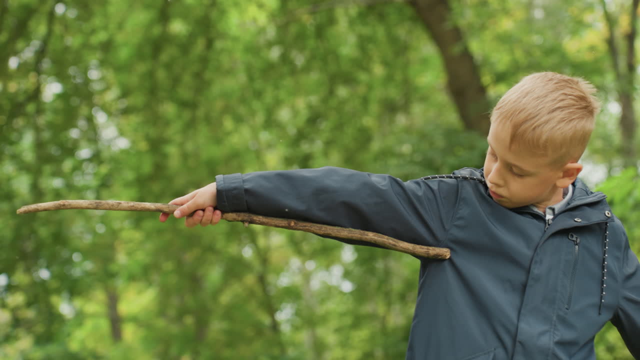 Junge übt vorgetäuschten Schwertkampf. Kind mit konzentriertem Blick hält Stock während eines fantasievollen Abenteuers. Junge übt sorgfältig vorgetäuschtes Schwertkämpfen mit einem Stock, bevor er zur Schule zurückkehrt