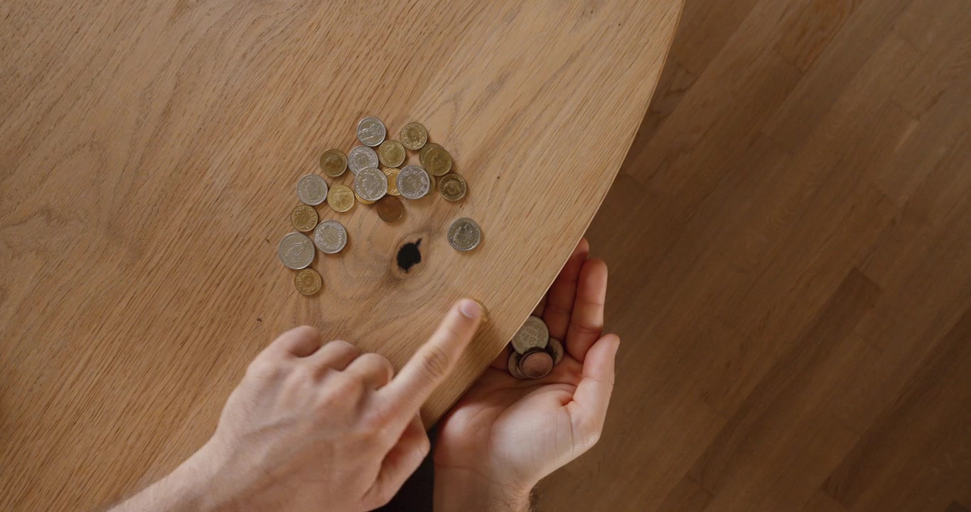 Vista dall'alto di una persona che conta monete su un tavolo di legno. Concetto finanziario di budgeting, risparmi, spese, finanza personale e gestione del denaro.