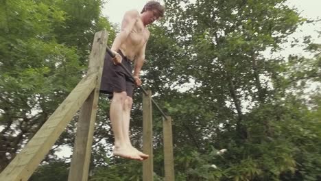 A young fit shirtless man performs muscle-up exercise outdoors on home gym