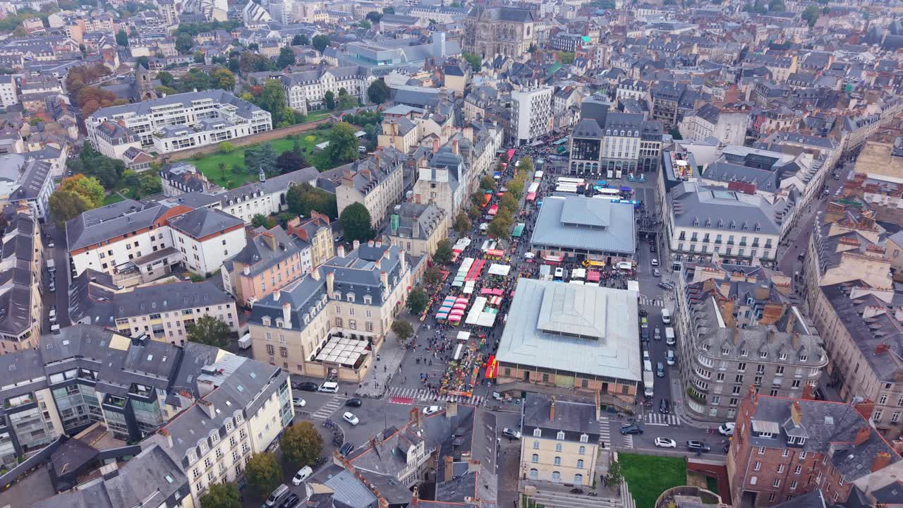 Drone shot in a downward view flying above the bustling market on Place des Lices in Rennes. Colorful stalls and busy streets are surrounded by the city’s historic buildings and rooftops