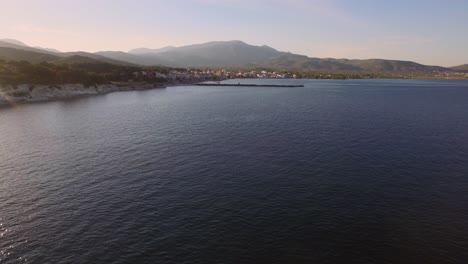 Aerial:-Small-fishing-town-with-Greek-flag-on-Samos-island,-Greece