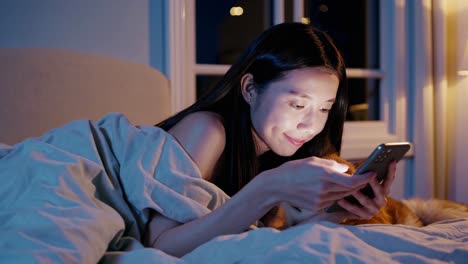 woman using phone in bed at night with dog