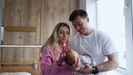 loving parents standing at the window with their tiny baby. happy mom and dad with a newborn in maternity hospital.