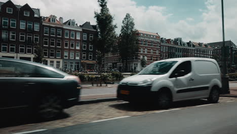 slow motion shot of a street scene in amsterdam, netherlands. parked cars in the foreground and old dutch architecture buildings in the background.