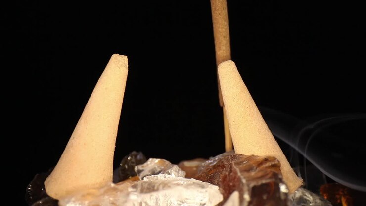 Allontanandosi da un bastoncino d'incenso fumante, oltre i coni d'incenso spenti in un giardino roccioso decorativo, utilizzando un obiettivo macro a sonda grandangolare per i dettagli fini di rocce e coni.