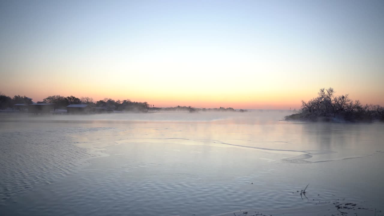 Steam coming off a partially frozen lake during sunrise.