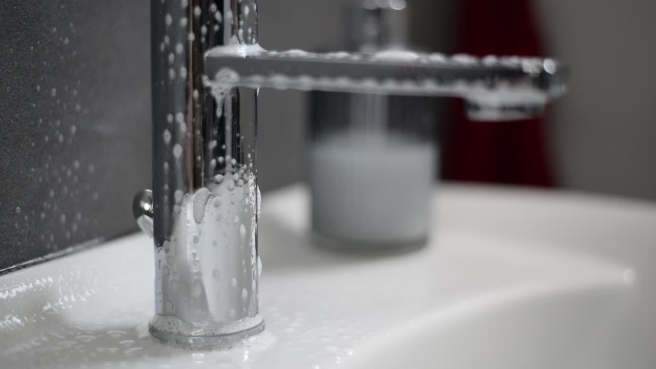 Un rubinetto cromato del lavandino del bagno viene spruzzato con un detergente