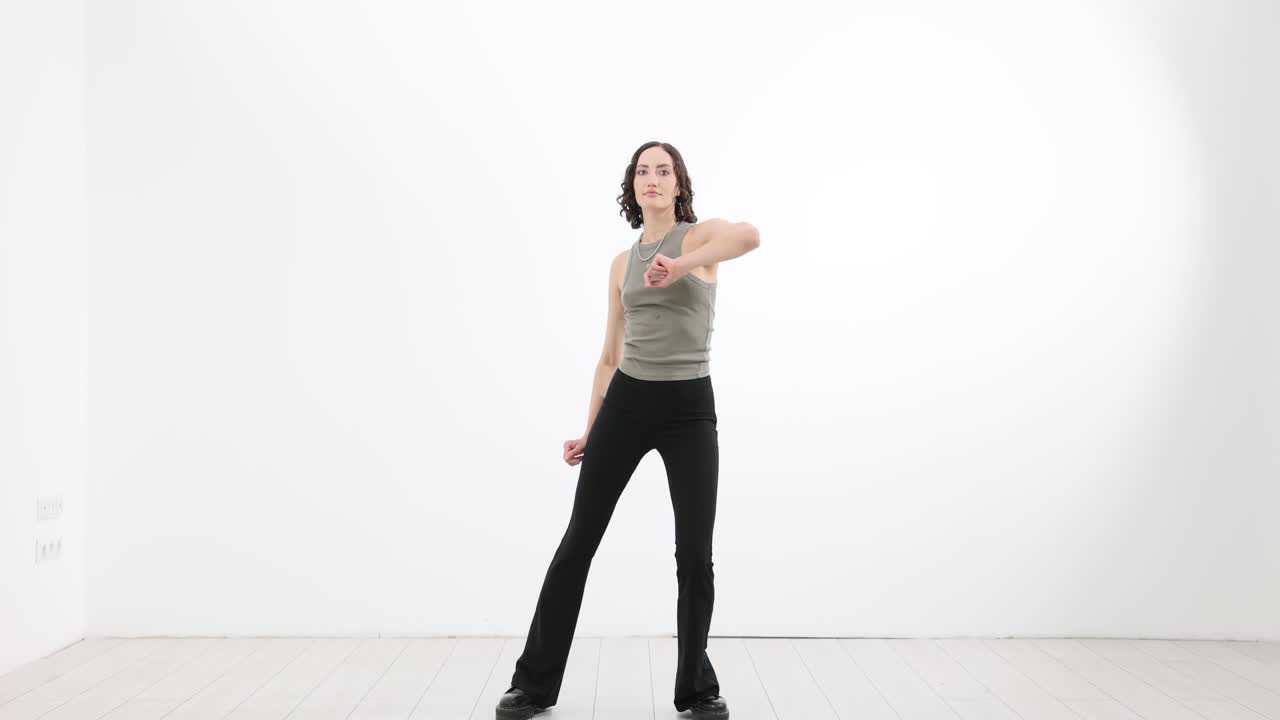 Una donna atletica balla con movimenti lenti e fluidi in uno studio bianco.
