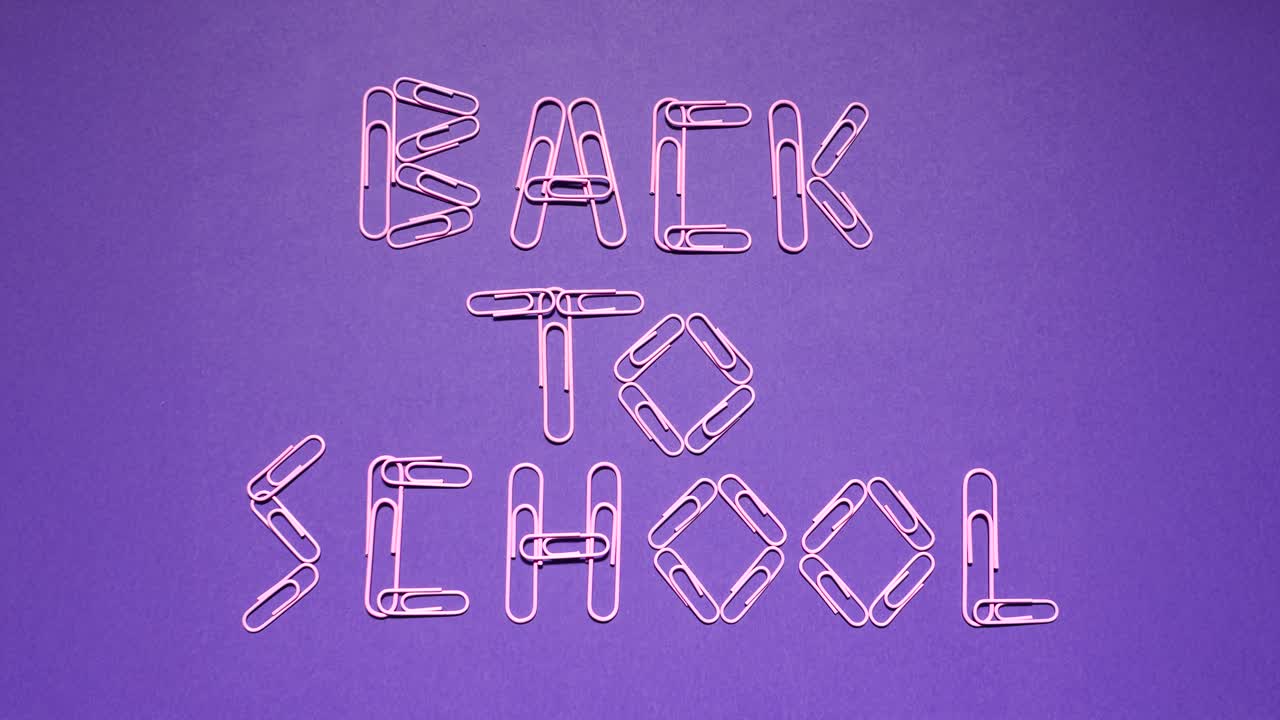 Looping stop-motion animation shows pink paper clips forming and scattering the words Back to School on a violet desk