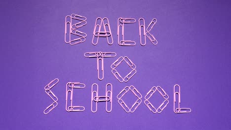 looping stop-motion animation shows pink paper clips forming and scattering the words back to school on a violet desk