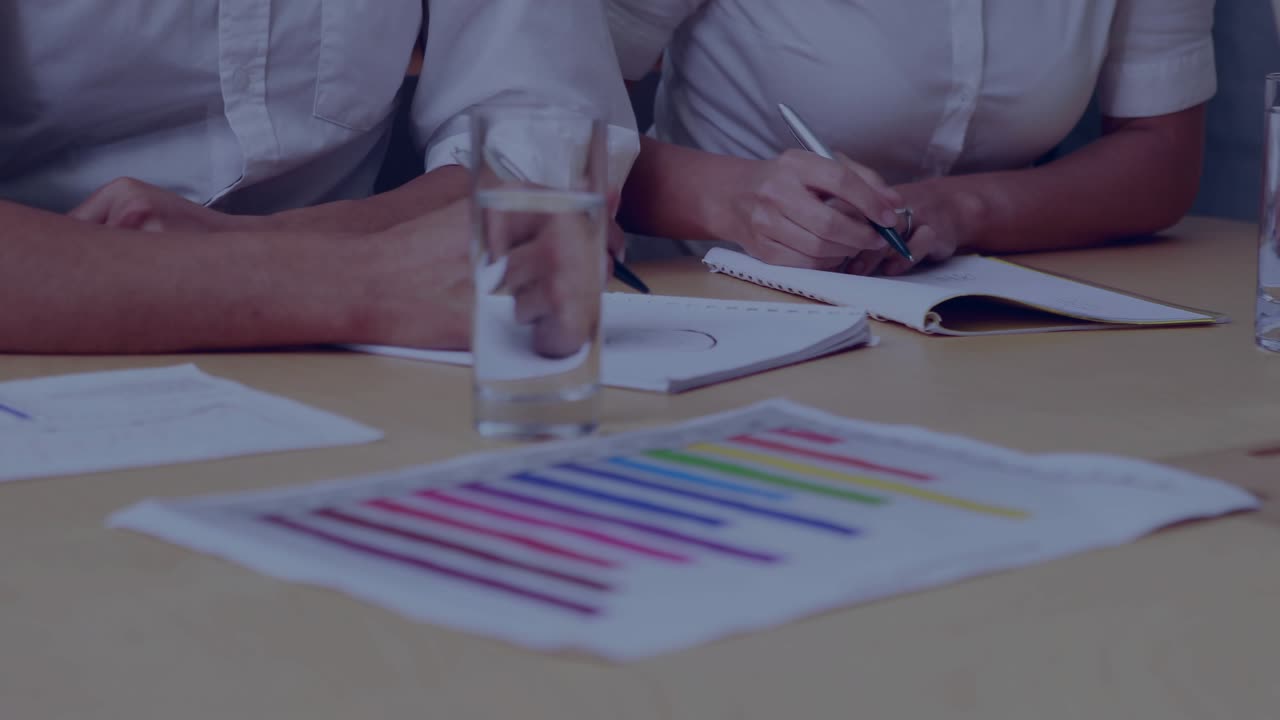 Two business colleagues reviewing bar chart, noting and initiating world map overlay over desk