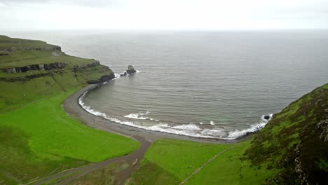 waves roll onto green coastline, talisker bay beach scotland, drone aerial shot