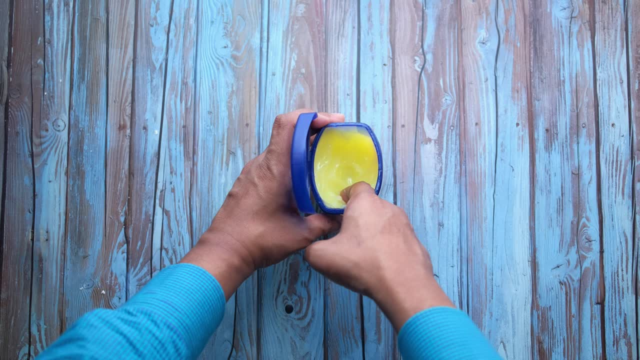 mano sosteniendo un frasco abierto de ungüento sobre un fondo de madera