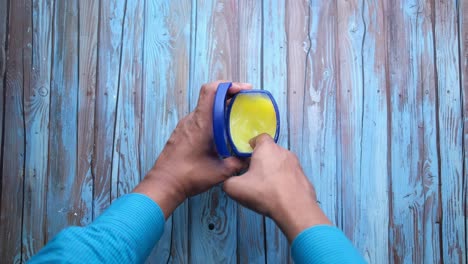 mano sosteniendo un frasco abierto de ungüento sobre un fondo de madera