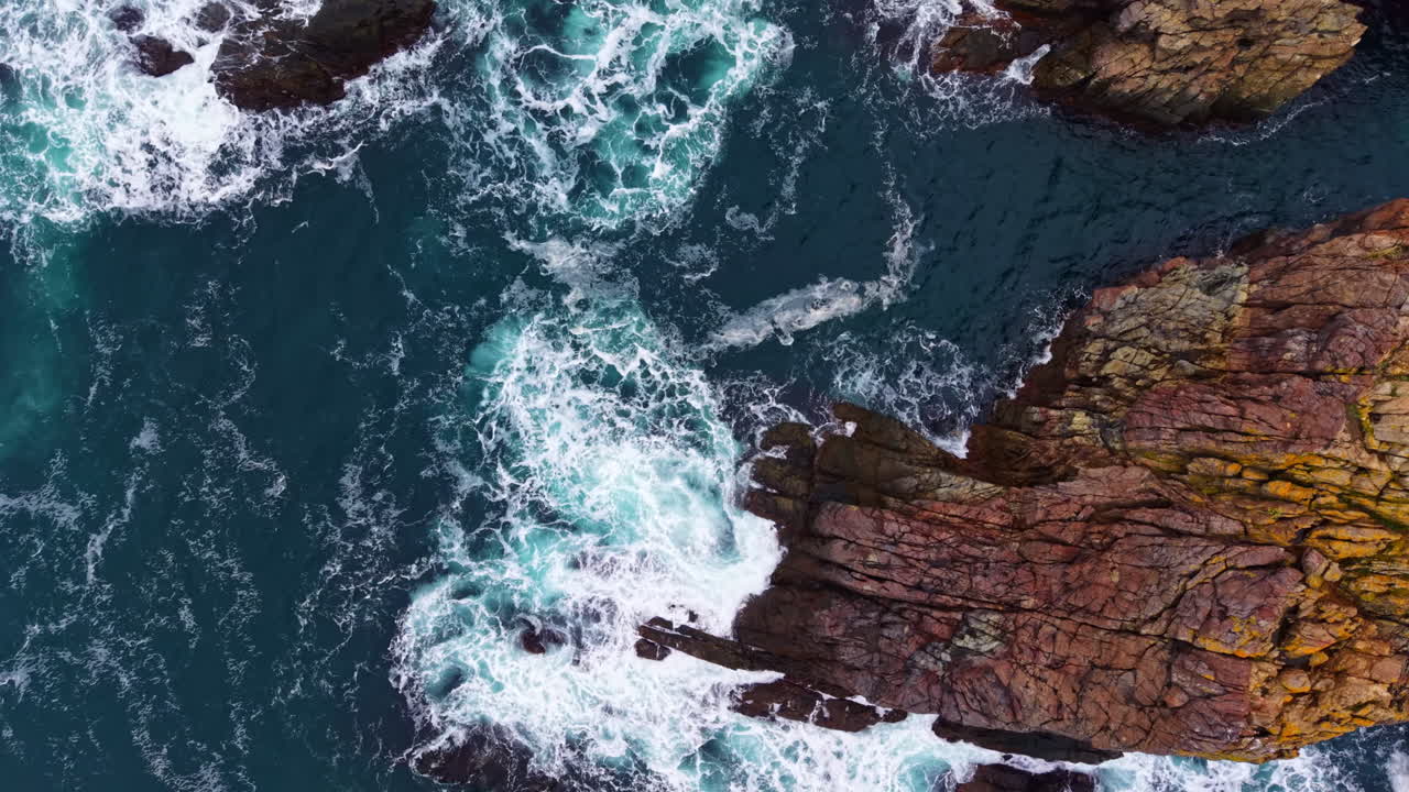 Waves crash against rugged cliffs at a coastal paradise, showcasing nature's raw beauty during a sunny afternoon by the sea