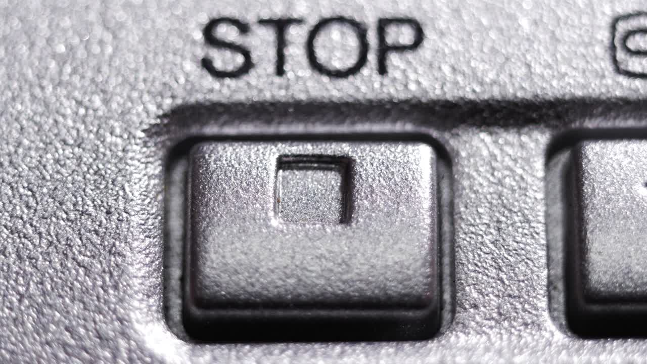 Close-up of a silver stop button with a square icon being pressed on a vintage media device