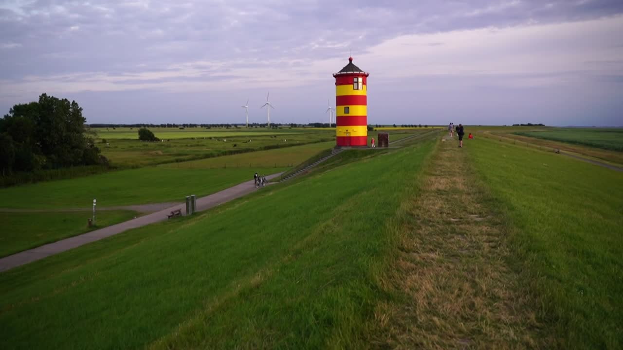 Panorerer til et lille gul-rødt fyrtårn i Nordtyskland på en klit ved havet.
