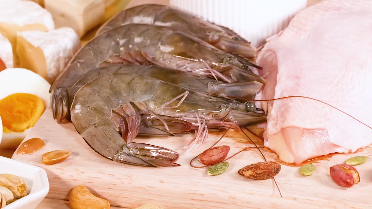 A variety of protein sources including shrimp, meats, nuts, and eggs displayed on a wooden surface.