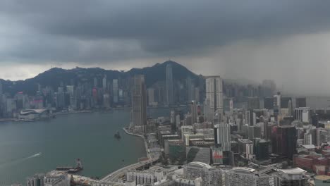 a sweeping aerial view captures hong kong's iconic skyline as a dramatic thunderstorm rolls in. the moody, overcast sky contrasts with the vibrant cityscape below