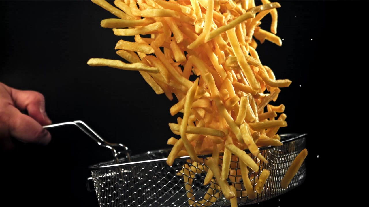 Goldene Pommes Frites werden in Zeitlupe vor schwarzem Hintergrund geworfen