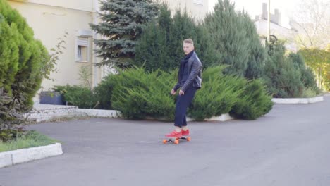 chłodny młody człowiek w skórzanej kurtce łyżwiarzem na swoim longboardzie