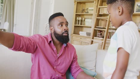 Serious-african-american-father-and-son-sitting-on-sofa-and-talking,-in-slow-motion