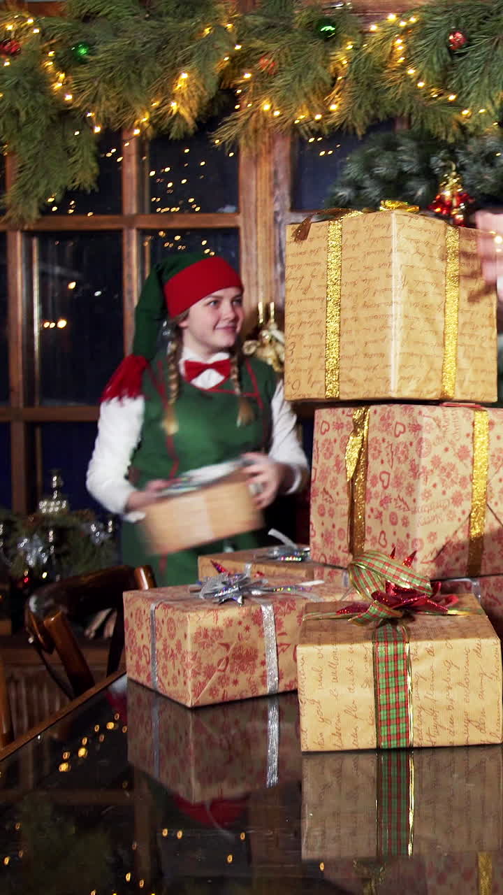Christmas gifts in Santa's residence. Elves making a pile of gift boxes on the table in beautifully decorated room with Christmas tree. Vertical video