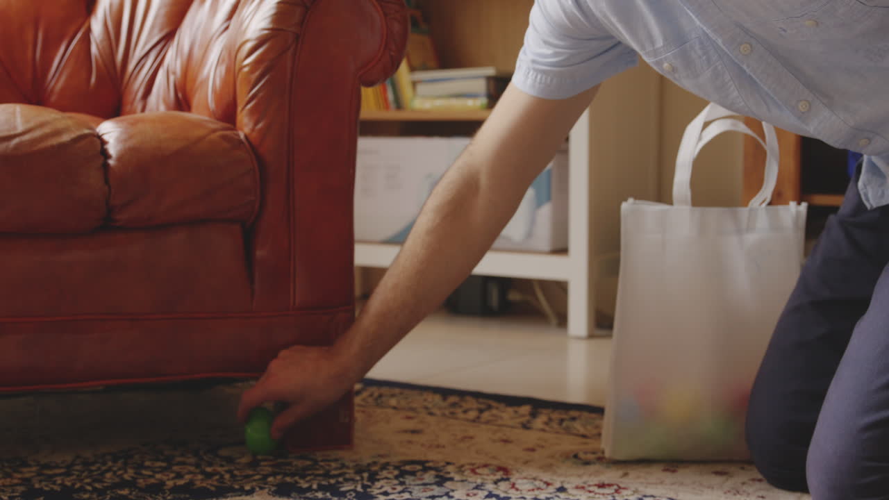 foto fija de una persona escondiendo un huevo de pascua verde debajo de un sofá de cuero marrón