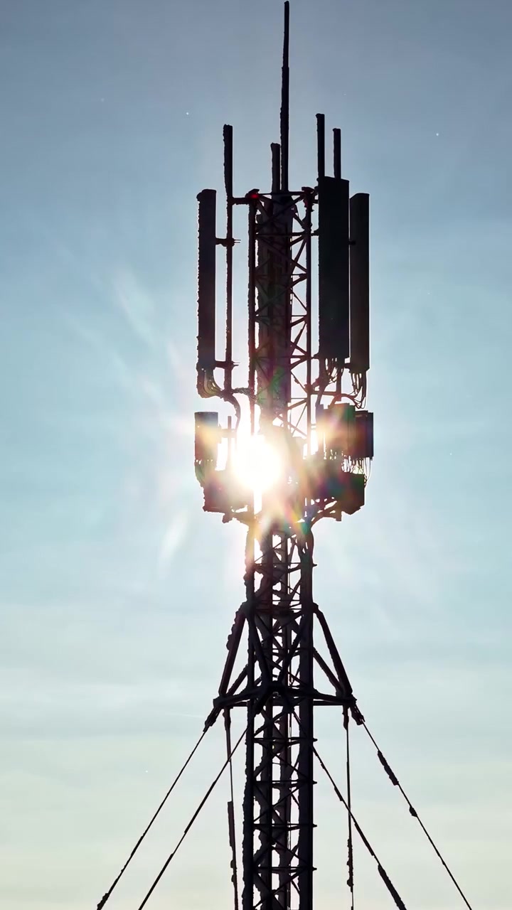 Il sole splende intensamente attraverso una torre di telecomunicazioni, creando una silhouette suggestiva contro un cielo sereno. Ideale per temi di tecnologia o comunicazione.