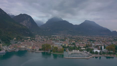 Toma-Aérea-Volando-Sobre-Riva-Del-Garda-Hacia-Las-Majestuosas-Montañas-En-Luz-Fría,-Suave-Y-Matutina