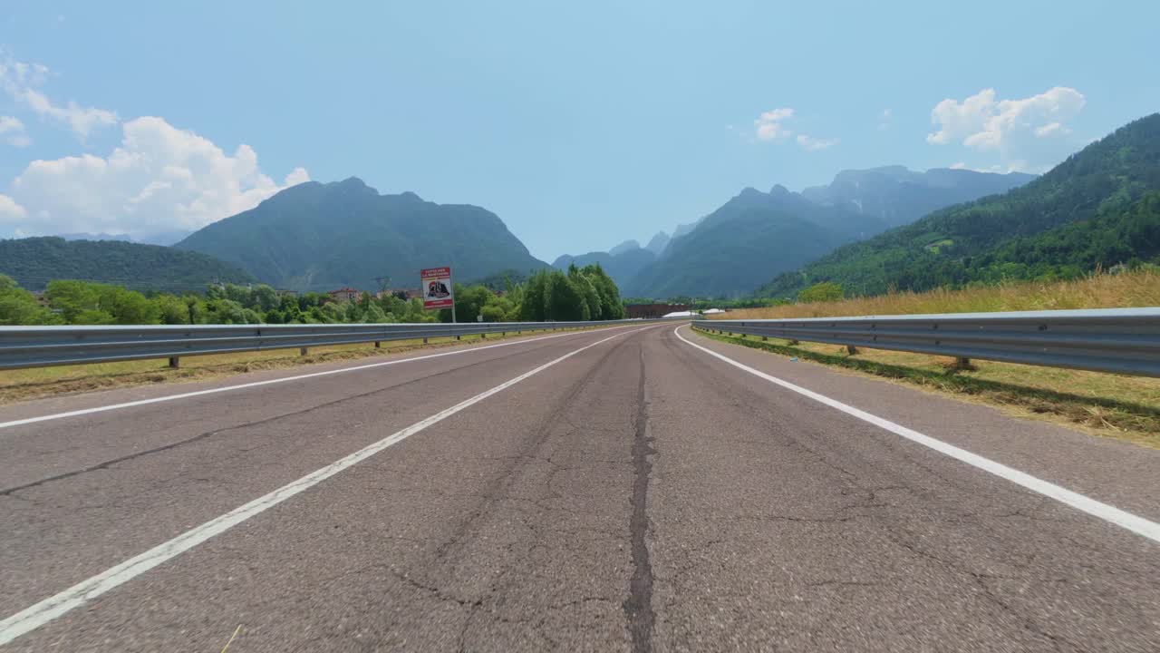 Winding asphalt road traversing scenic mountain valley in dolomites, surrounded by lush green vegetation under bright blue sky with scattered clouds, capturing alpine landscape beauty