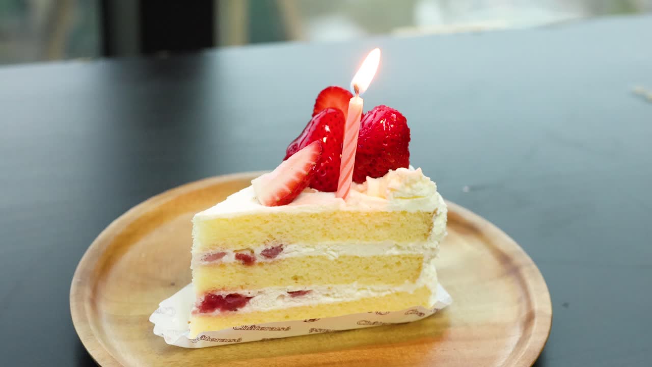 Single strawberry shortcake slice with candle burning, natural daylight, static camera, minimal movement