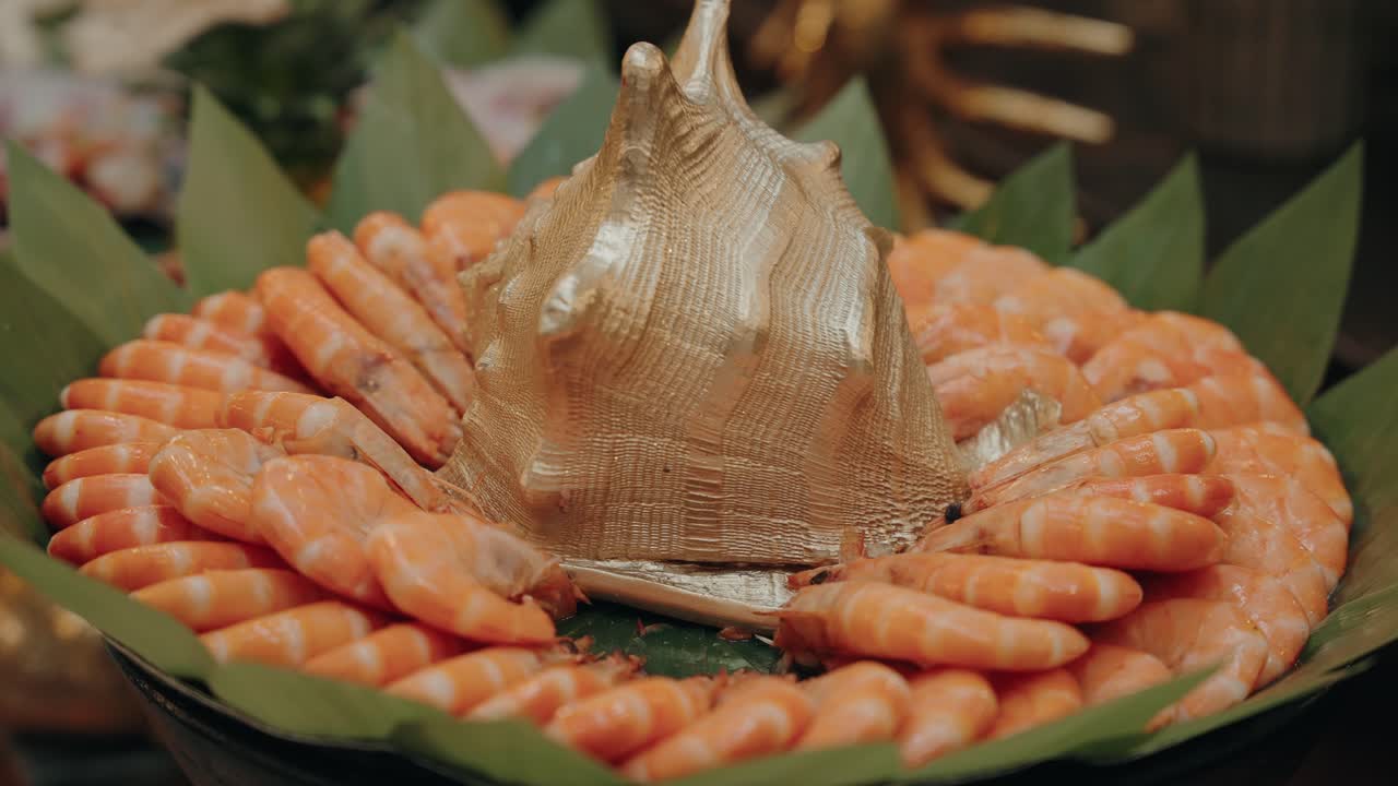 cooked prawns arranged around gold seashell centerpiece on leaf platter