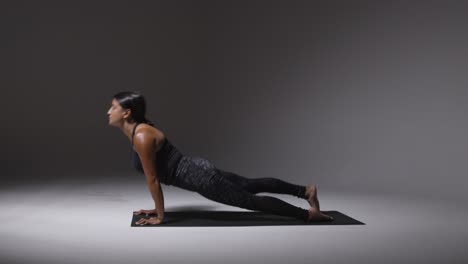 studio shot of mature woman wearing gym fitness clothing standing on mat doing variety of pilates stretching exercises 1